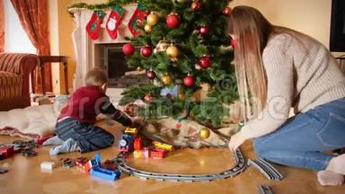 小男孩在客厅圣诞树下和他母亲玩玩具火车和铁路的4K视频。 儿童